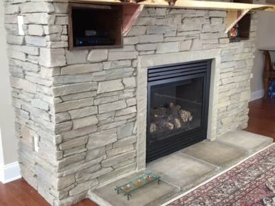 A closeup of a grey stonework fireplace with a hearth extension of flat, grey stones.