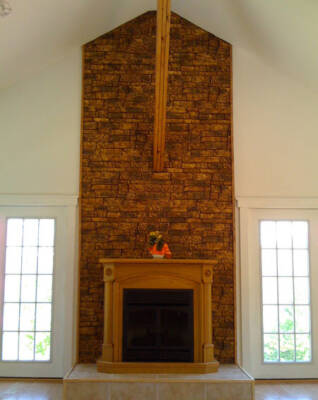 A wood-framed fireplace sits against a floor-to-ceiling accent wall of reddish-brown stonework. The fireplace sits in an open room between two french doors.