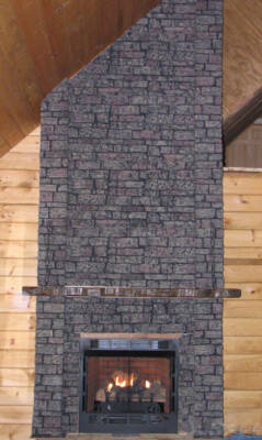Rustic living room featuring wood panel walls and a fireplace with dark grey, floor-to-ceiling stonework.