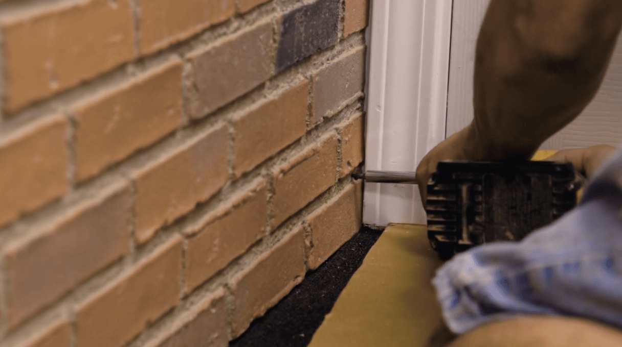 Close up shot of a person using a drill to attach a red brick faux wall panel to a wall.