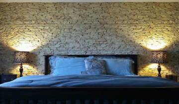 Bedroom with a king bed and two lamps against a wall of stacked stone decorative wall panels.
