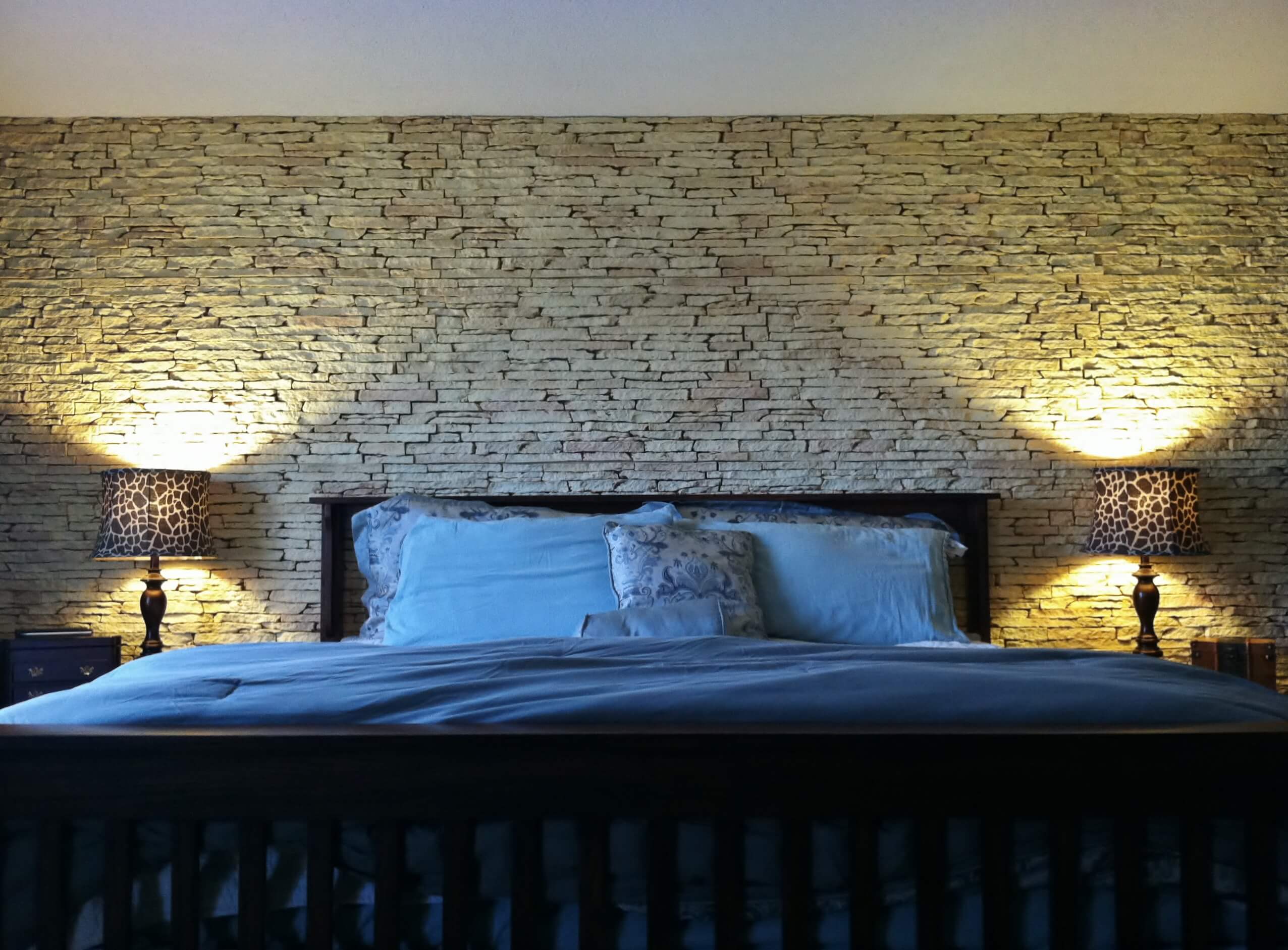 Bedroom with a king bed and two lamps against a wall of stacked stone decorative wall panels.