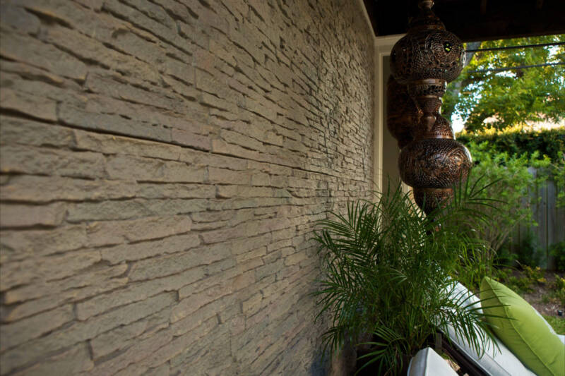 Side shot of an outdoor patio, with ferns and lounge chairs against an accent wall of ledgestone faux wall panels.