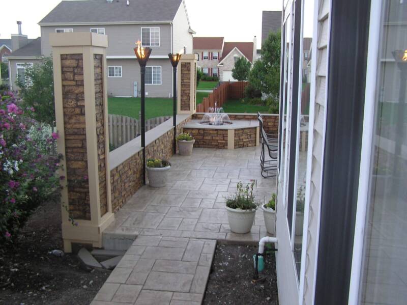 Outdoor patio with a water feature, constructed of stone tile flooring and brown stone faux wall panels.