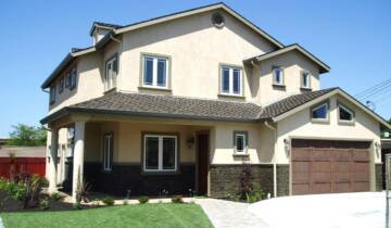 photograph of the front of a tan house with brown garage doors and a small patch of green grass in front