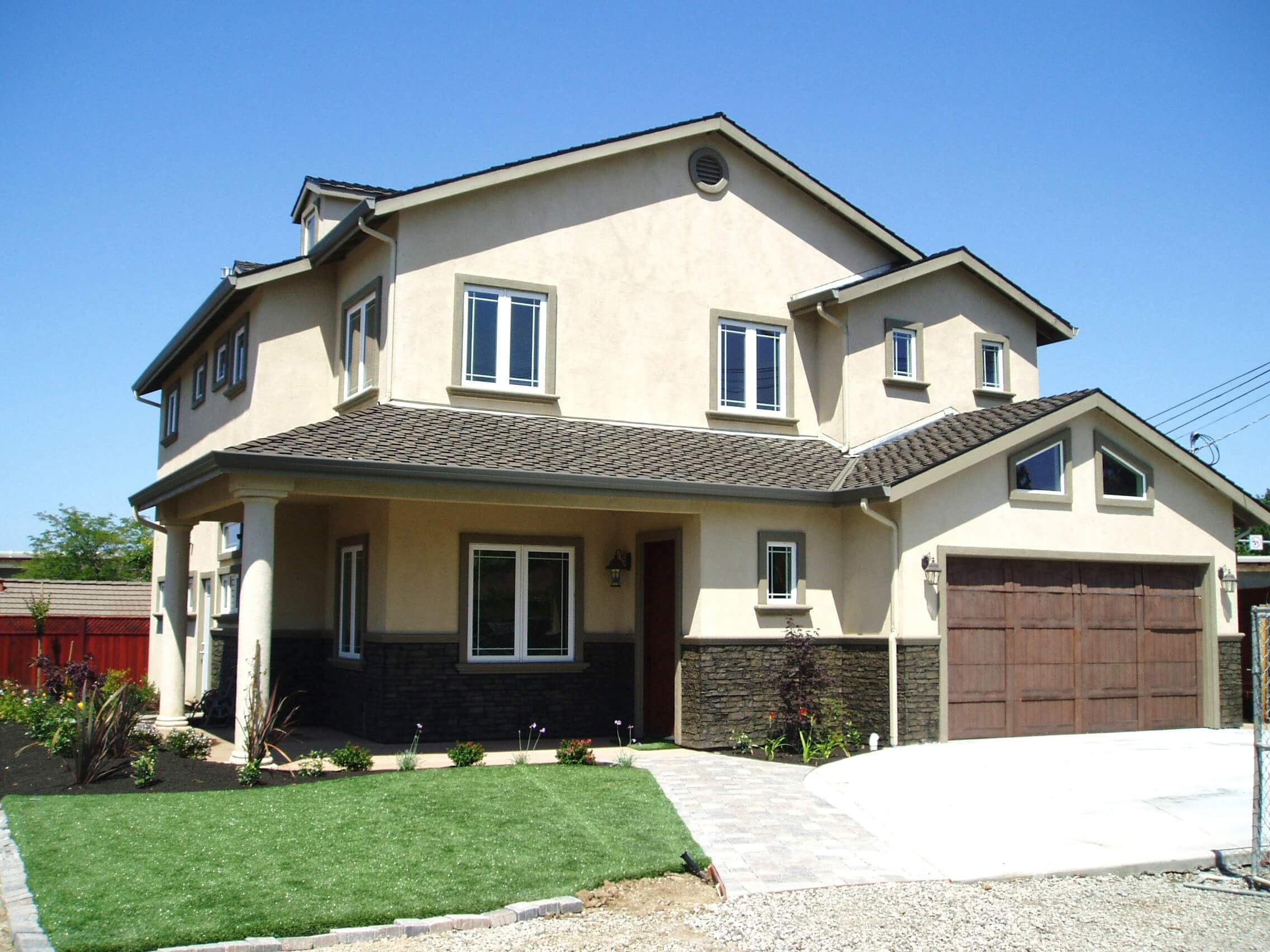 photograph of the front of a tan house with brown garage doors and a small patch of green grass in front