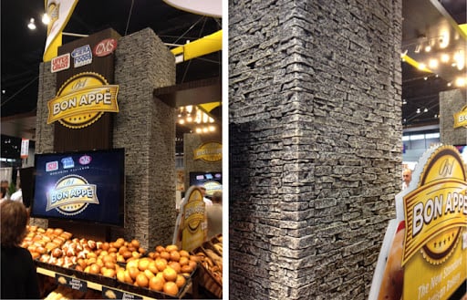 A large stand covered in gray faux stone panels, attached to trays with buns, rolls and other baked goods.