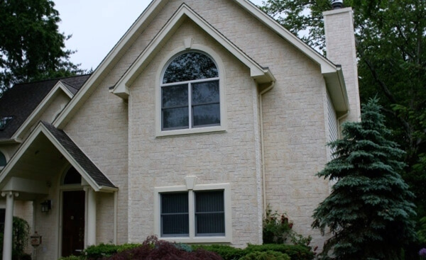Home exterior featuring a whitewashed faux stone facade. The home is surrounded by greenery, including shrubbery underneath a downstairs window.